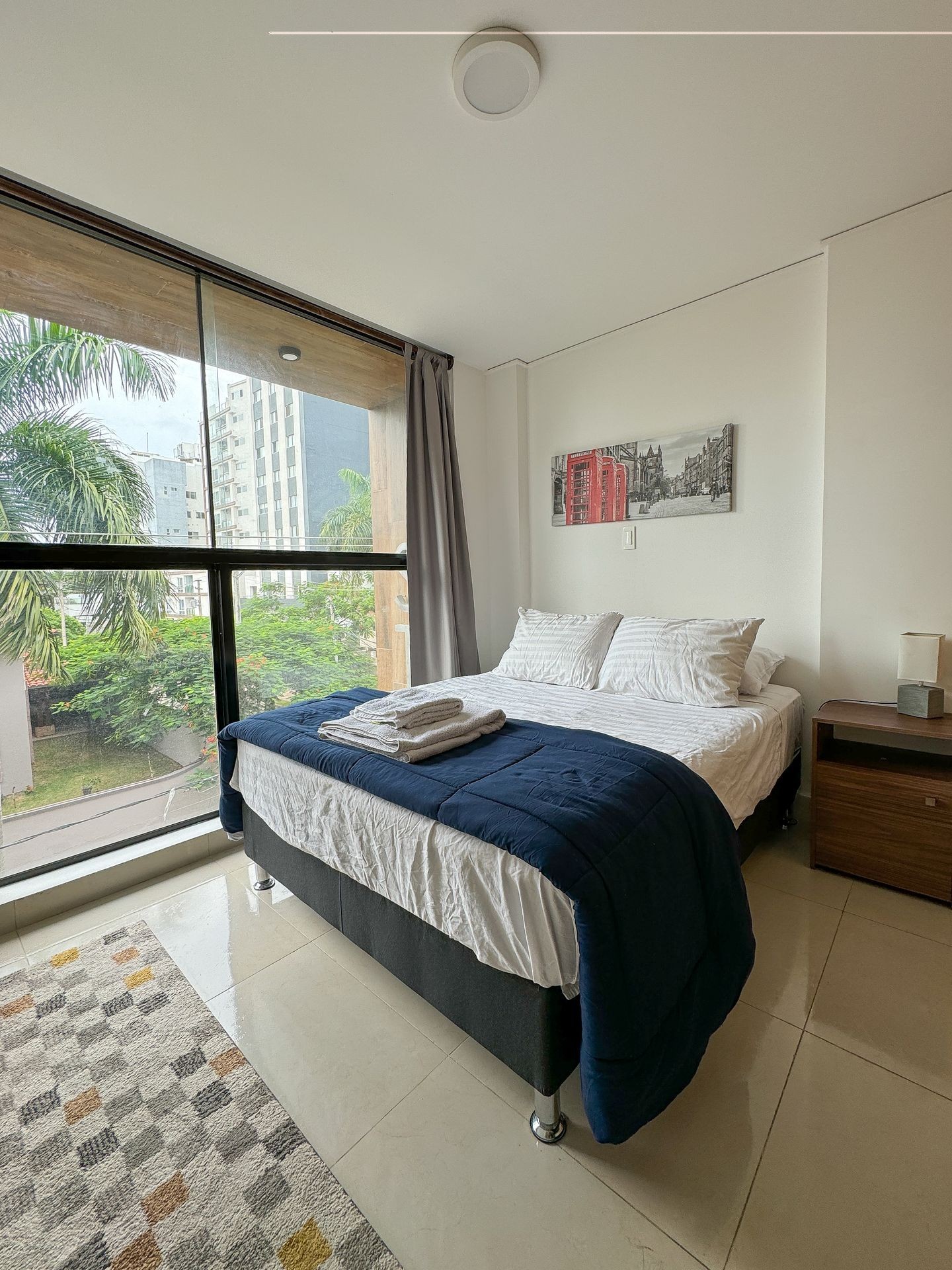 Modern bedroom with large windows, double bed, and urban view.