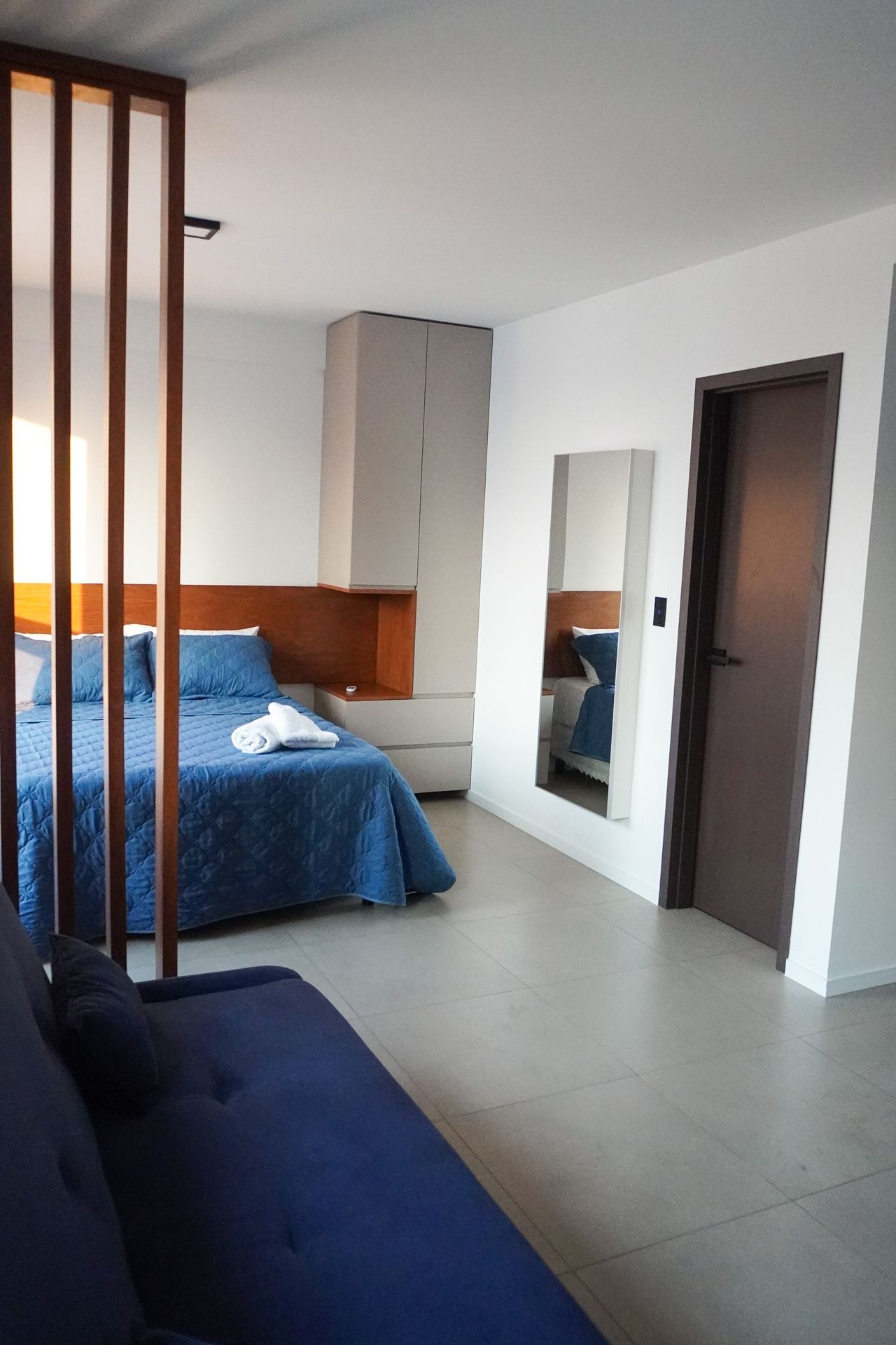 Modern bedroom with blue bedding, wooden accents, and a mirror beside a closed door.